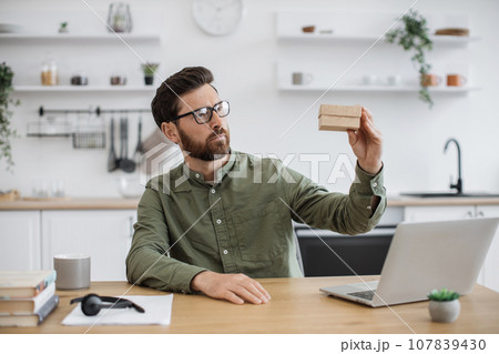 Focused vlogger sitting at desk and holding cardboard parcel Focused vlogger sitting at desk and holding cardboard parcel 107839430