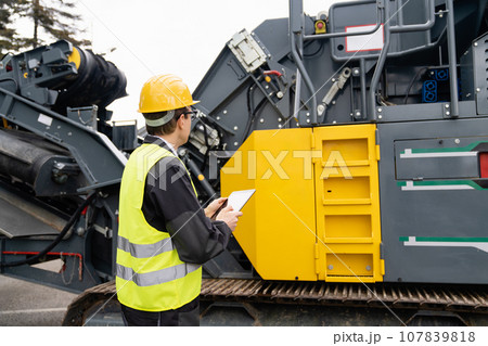 Engineer with digital tablet next to road construction machine Engineer with digital tablet next to road construction machine 107839818