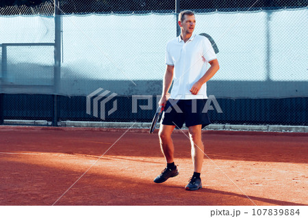 Young man plays tennis outdoors on tennis court in the morning Young man plays tennis outdoors on tennis court in the morning 107839884