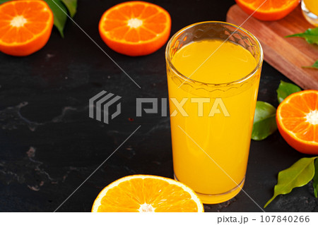 Glass of orange juice and cut oranges on table 107840266