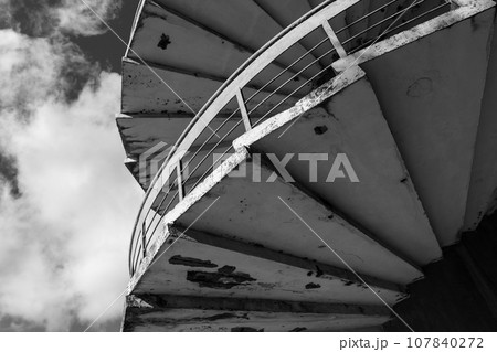 Grungy spiral ladder is under cloudy sky, abstract architectural photo 107840272