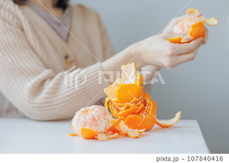 European woman cleans tangerines with her hands at home. citrus vitamins to boost immunity European woman cleans tangerines with her hands at home. citrus vitamins to boost immunity 107840416
