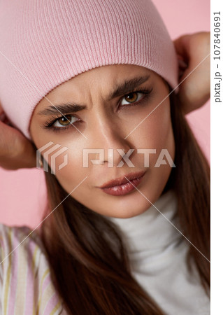 playful woman keeps hands on pink hat on pink background. playful woman keeps hands on pink hat on pink background. 107840691