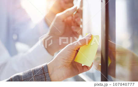 Hands of man sticking adhesive notes on glass 107840777