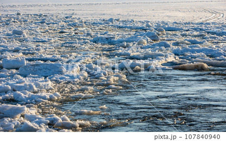 Thick white snow-covered ice floes float along the river. Spring ice drift. Thick white snow-covered ice floes float along the river. Spring ice drift. 107840940