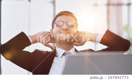 business man holding his hands behind his head while working on a laptop business man holding his hands behind his head while working on a laptop 107842773