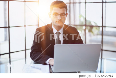 handsome business man in an elegant black suit at a laptop handsome business man in an elegant black suit at a laptop 107842793