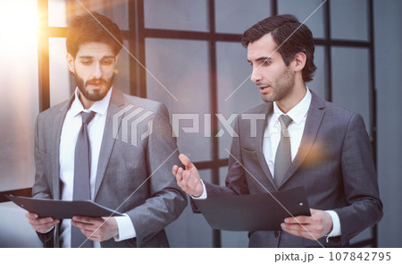 Rear view of two businessmen as they stare out a large window with a city view. 107842795