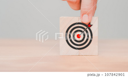 Hand put a goal icon on wooden cube block on wood table. Business concept of growth and goals in next year, targets, objectives, business success, planning, achievement, KPI and OKR. Hand put a goal icon on wooden cube block on wood table. Business concept of growth and goals in next year, targets, objectives, business success, planning, achievement, KPI and OKR. 107842901