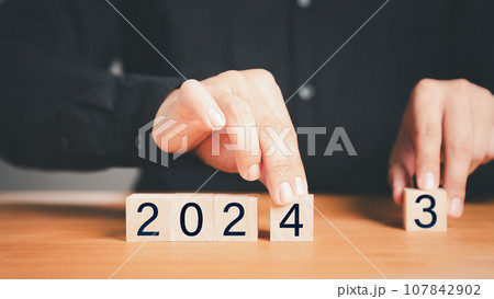 Male hand holding a wooden cube block with numbers 2024 on wood table. Goal in the new year 2024. Business development strategy, advancement and goal concept. Male hand holding a wooden cube block with numbers 2024 on wood table. Goal in the new year 2024. Business development strategy, advancement and goal concept. 107842902