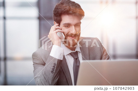 Happy young businessman talking on smart phone at desk in office 107842903