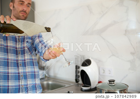 Details on hands of a handsome young adult Caucasian bearded man pouring wine into a glass from a bottle Details on hands of a handsome young adult Caucasian bearded man pouring wine into a glass from a bottle 107842989