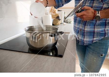 Close-up male chef seasoning and adding salt into stainless steel saucepan with boiling water standing on electric stove Close-up male chef seasoning and adding salt into stainless steel saucepan with boiling water standing on electric stove 107842995
