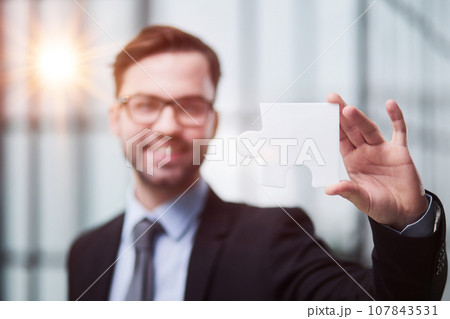 Portrait of optimistic bearded businessman holding puzzle pieces, solving tasks, looking at camera Portrait of optimistic bearded businessman holding puzzle pieces, solving tasks, looking at camera 107843531