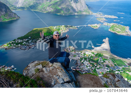 Relaxed happy hiker enjoys stunning views on Reinebringen peaks of Lofoten islands, fjords, Norway Relaxed happy hiker enjoys stunning views on Reinebringen peaks of Lofoten islands, fjords, Norway 107843646