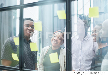 a team of young designers sticking notes on glass in a modern office a team of young designers sticking notes on glass in a modern office 107844877