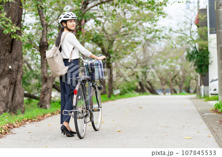サイクリングヘルメットをかぶって自転車を引いて歩く若い女性 サイクリングヘルメットをかぶって自転車を引いて歩く若い女性 107845533