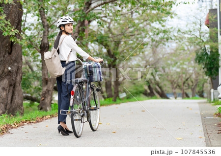 サイクリングヘルメットをかぶって自転車を引いて歩く若い女性 サイクリングヘルメットをかぶって自転車を引いて歩く若い女性 107845536