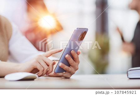 Cheerful student woman sitting at table break holding mobile phone surfing internet 107845921