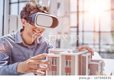 man sits in the office of a realtor and looks at the layout of the apartment in virtual reality glasses. man sits in the office of a realtor and looks at the layout of the apartment in virtual reality glasses. 107846830