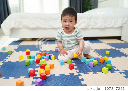 happy infant baby playing wooden block toy on jigsaw mat in bedroom 107847241
