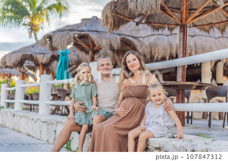 A happy, mature couple over 40 with their two daughters, enjoying a leisurely walk in a park, their joy evident as they embrace the journey of pregnancy later in life 107847312
