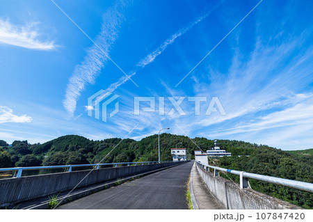 2023秋奈良市の水がめ布目ダム　ダム上の道路と上空の飛行機雲 107847420