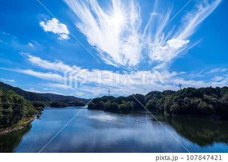 2023秋奈良市の水がめ布目ダム　ダム湖の上空で燦然と輝く太陽と水面のリフレクション② 107847421