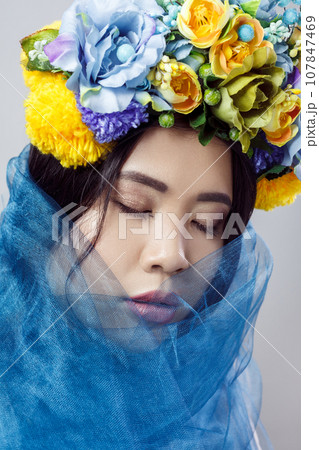 Portrait of sensual attractive woman with beautiful makeup , dark hair, with floral hat and blue veil, posing with closed eyes, expressing gentle. Indoor studio shot isolated on gray background, 107847469