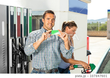 Smiling man and woman in gas station, demonstrating gas credit card Smiling man and woman in gas station, demonstrating gas credit card 107847601