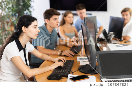 Girl student of computer courses looks at monitor screen, types on keyboard and does work Girl student of computer courses looks at monitor screen, types on keyboard and does work 107847825