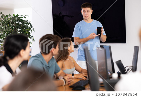 Young male speaker holds mobile phone in hands and explains to listeners of computer courses 107847854