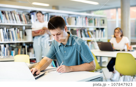 Concentrated young man checking plans in calendar while studying in the library and using laptop 107847923
