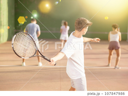 Guy hits the ball with a racket while playing frontenis on outdoor court Guy hits the ball with a racket while playing frontenis on outdoor court 107847986
