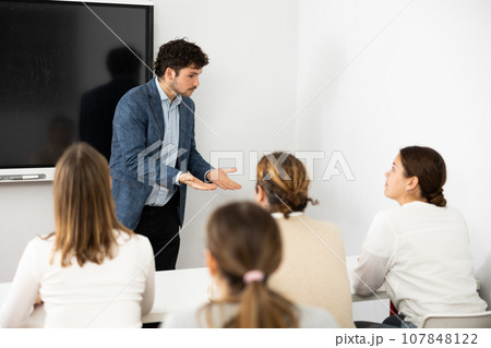 Positive male trainer, conducting advanced training courses to office employees sitting at desks in auditory 107848122