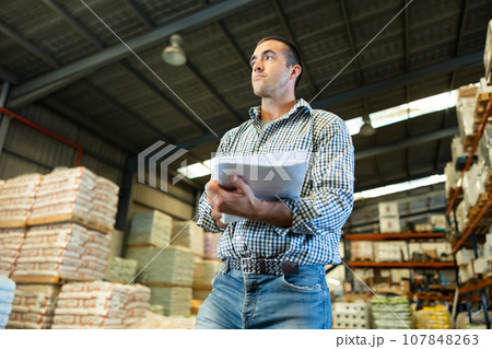 Man standing in warehouse and verifying documents with presence of goods in the warehouse of industrial goods 107848263