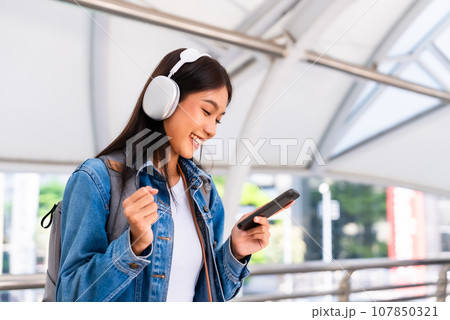 Portrait of happy young asian woman listening music online with wireless headphones Portrait of happy young asian woman listening music online with wireless headphones 107850321