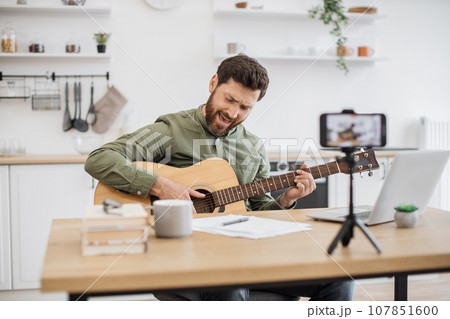 Inspired man playing guitar while recording video on mobile 107851600