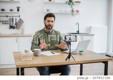Man working on laptop and recording video on smartphone Man working on laptop and recording video on smartphone 107852186
