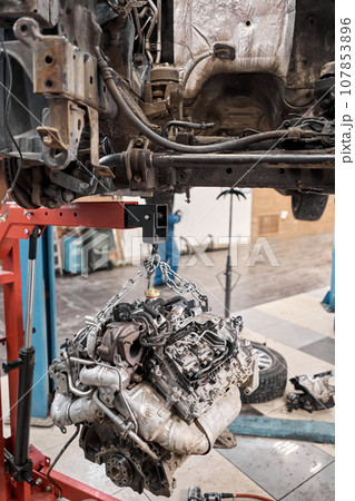 A car mechanic inspects the engine with a flashlight. Engine Block on a repair stand with Special crane jack. Technical service station for car. 107853896