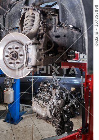 A car mechanic inspects the engine with a flashlight. Engine Block on a repair stand with Special crane jack. Technical service station for car. A car mechanic inspects the engine with a flashlight. Engine Block on a repair stand with Special crane jack. Technical service station for car. 107853898