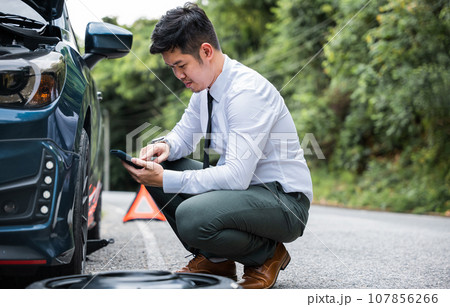 Portrait man sitting while calling roadside assistance after breaking down. Elegant middle age businessman wearing white shirt and waiting for help car accident on road. Roadside assistance concept. 107856266