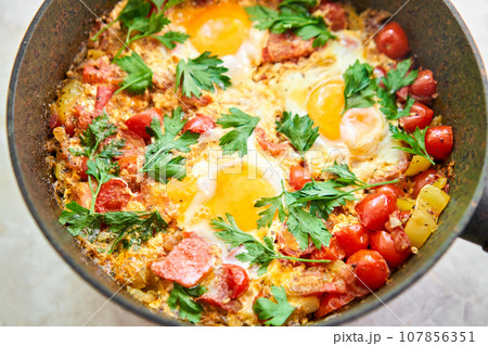 Shakshouka for breakfast. Homemade shakshuka, fried eggs, onion, bell pepper, tomatoes and parsley in a pan. Marble background. Top view. chakchouka Shakshouka for breakfast. Homemade shakshuka, fried eggs, onion, bell pepper, tomatoes and parsley in a pan. Marble background. Top view. chakchouka 107856351