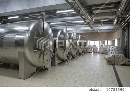 Large modern wine barrels at the winery, the concept of a large factory, production. Silver colored barrels, silver pipes on the ceiling. 107856994