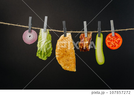 Doner kebab with ingredients hanging on a thread in the air : beef meat, lettuce, onion, tomatoes, cheese, cucumber. Black background Doner kebab with ingredients hanging on a thread in the air : beef meat, lettuce, onion, tomatoes, cheese, cucumber. Black background 107857272