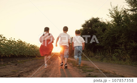 Little boys and girl run playing together along road at sunset countryside Little boys and girl run playing together along road at sunset countryside 107857358