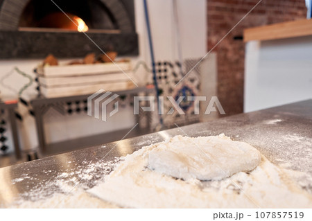 pizza dough in the foreground. A wood-burning stove in the background. Neapolitan pizza. pizza dough in the foreground. A wood-burning stove in the background. Neapolitan pizza. 107857519