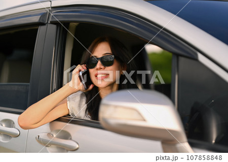Beautiful woman talking on mobile phone while driving a car and looking on the road through the window Beautiful woman talking on mobile phone while driving a car and looking on the road through the window 107858848