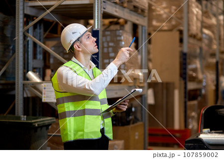 male worker doing stocktaking of product management on shelves in warehouse, counting 107859002