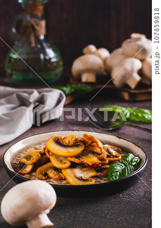 Appetizing fried champignons and basil leaves on a plate on the table vertical view 107859818